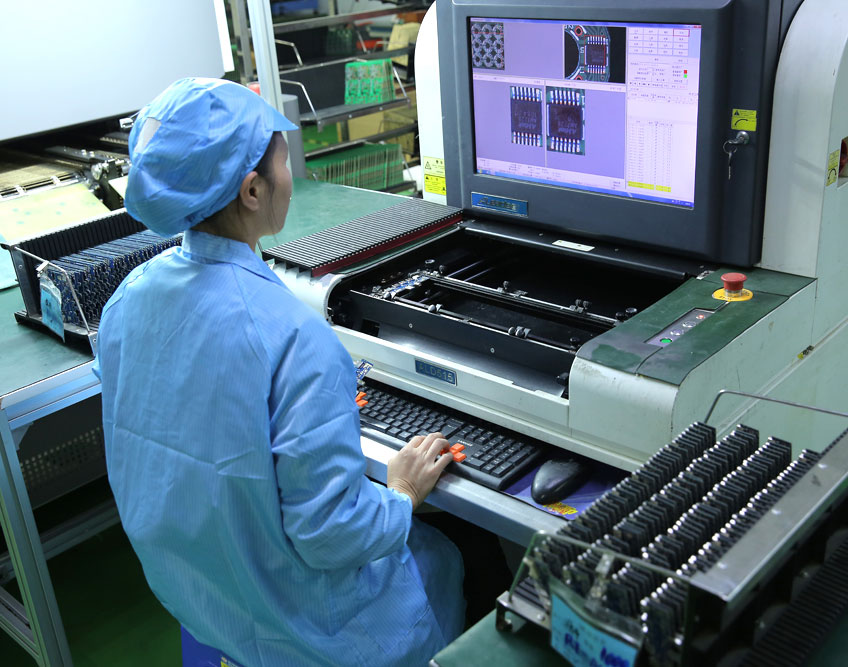 Operator reviewing circuit board inspection images at a workstation beside racks of boards